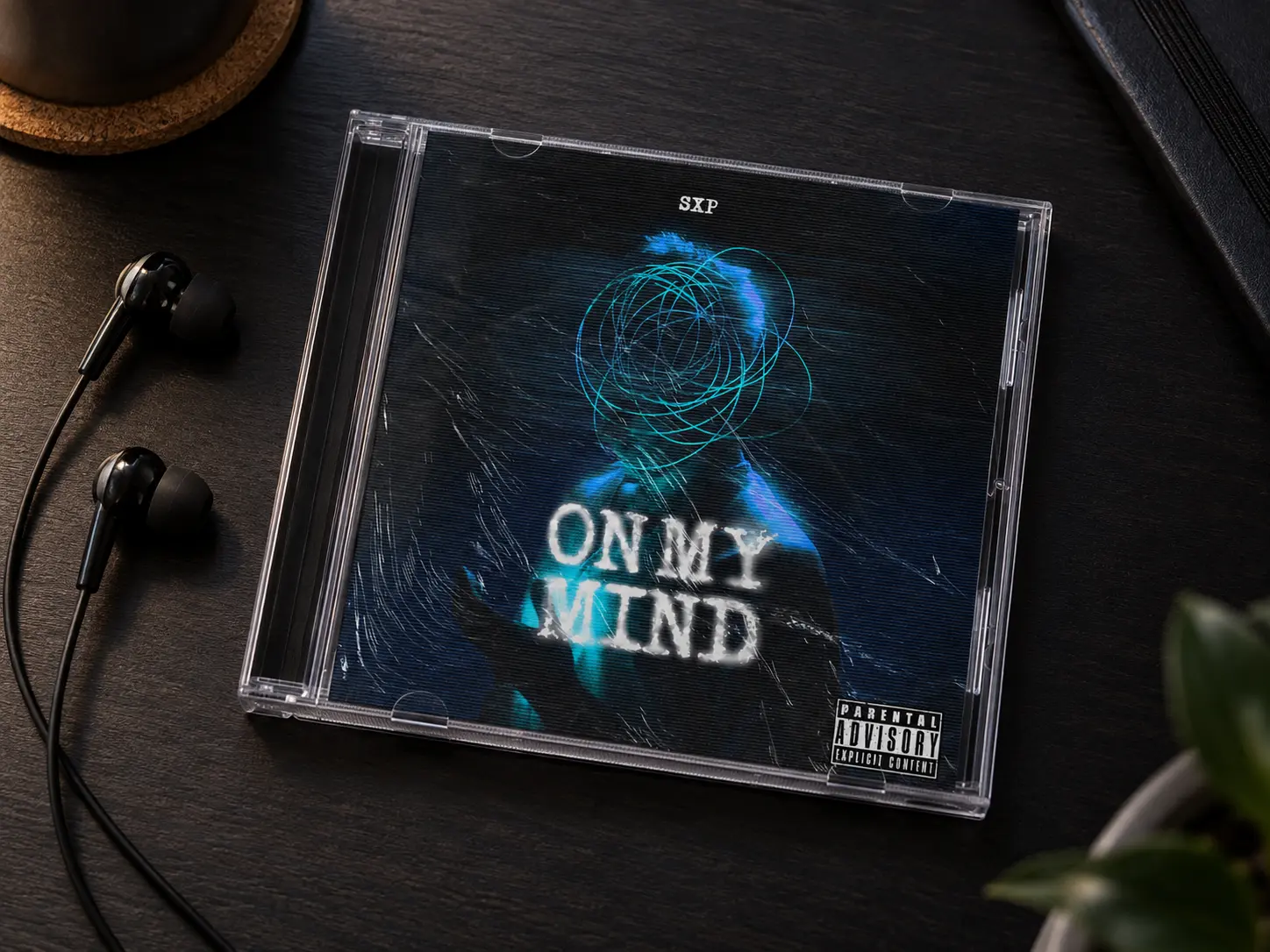 A clear CD jewel case with the On My Mind cover, lying on a dark desk beside wired earphones.