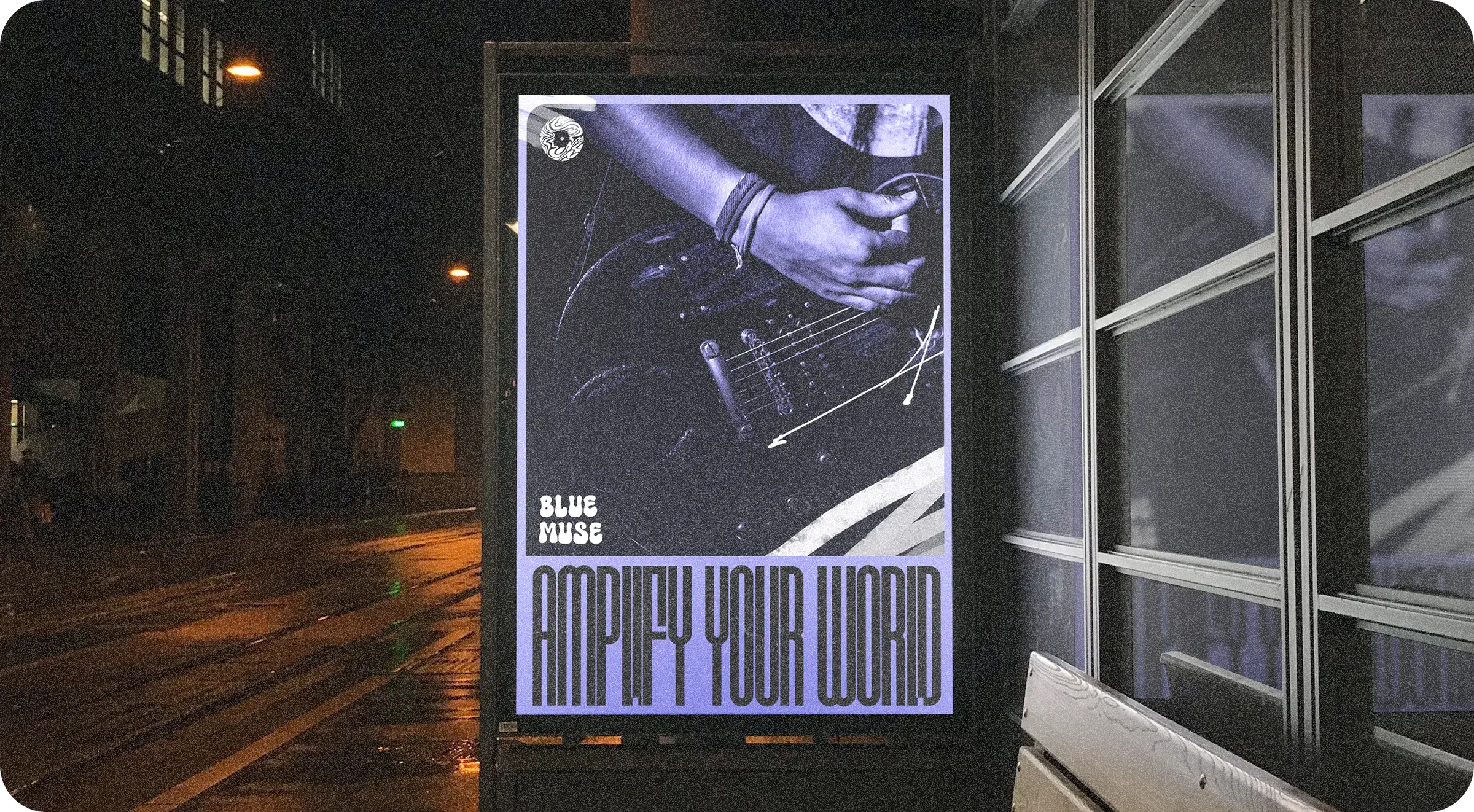 A poster in a bus shelter at night: a guitarist’s hands in violet duotone, the logo, and AMPLIFY YOUR WORLD in tall letters.