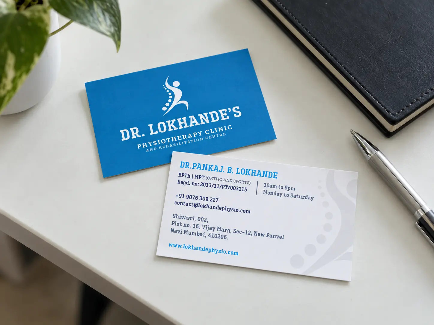 Dr. Lokhande's visiting cards, the blue front with the spine mark and the white back with his details, on a clinic reception desk.