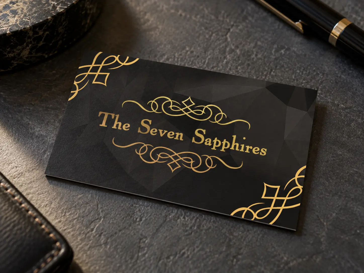 A Seven Sapphires business card face up on a dark slate desk: the black front with the gold logo between its flourishes