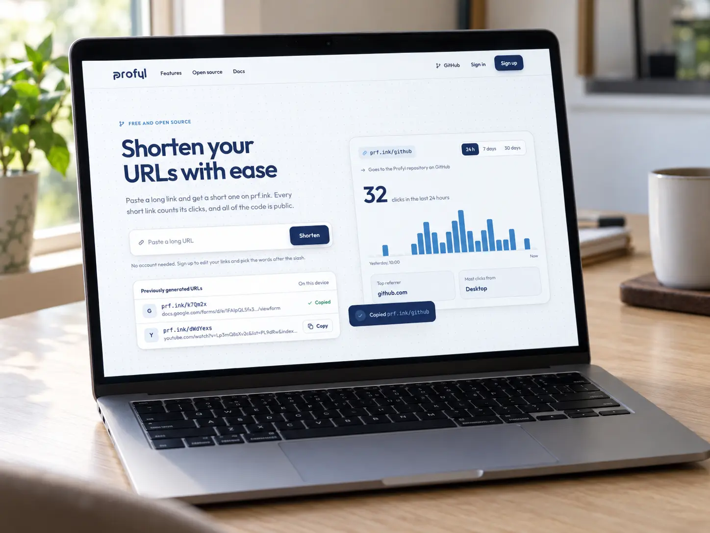 A laptop on a pale oak desk showing Profyl's home page: Shorten your URLs with ease, a box for a long link and a card counting 32 clicks in the last 24 hours.
