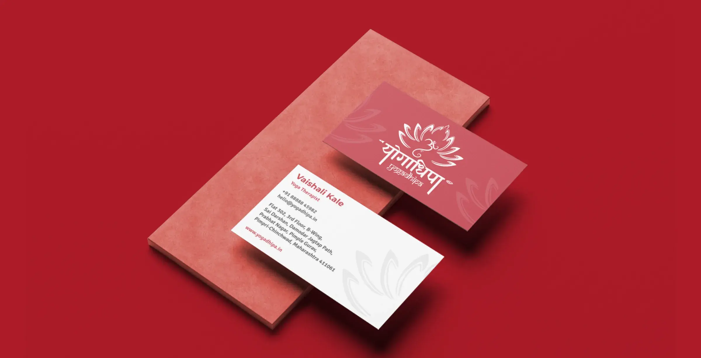 Two Yogadhipa visiting cards on a red textured block: the red front with the white logo, and the white back with the therapist’s details.