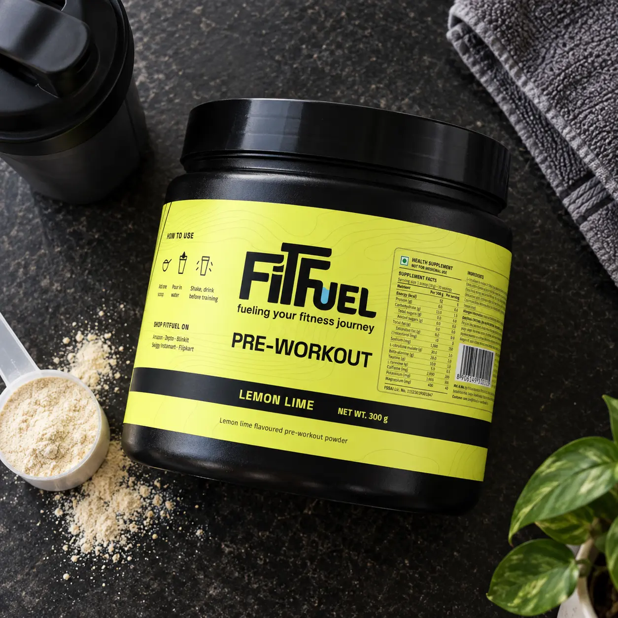 A FitFuel pre-workout tub in its lime label on a black counter, a scoop of powder beside it